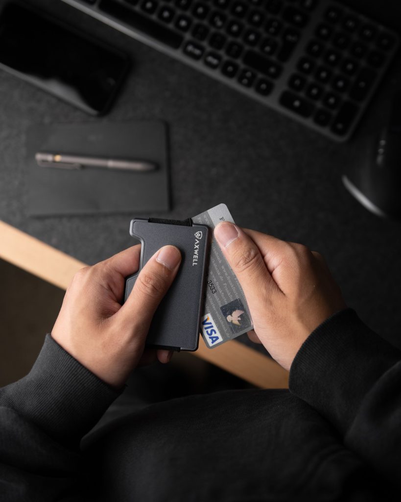 A close-up of hands holding a sleek minimalist metal wallet containing ID and credit card.