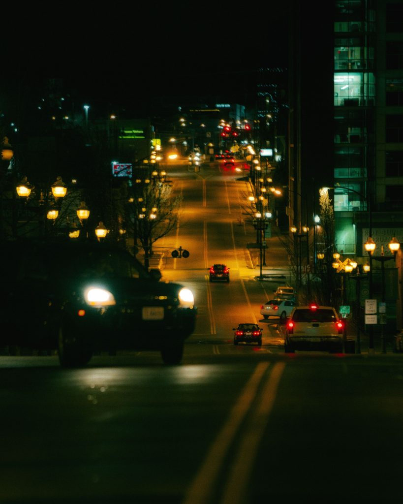 A moody urban street scene at night featuring moving vehicles and vibrant city lights.